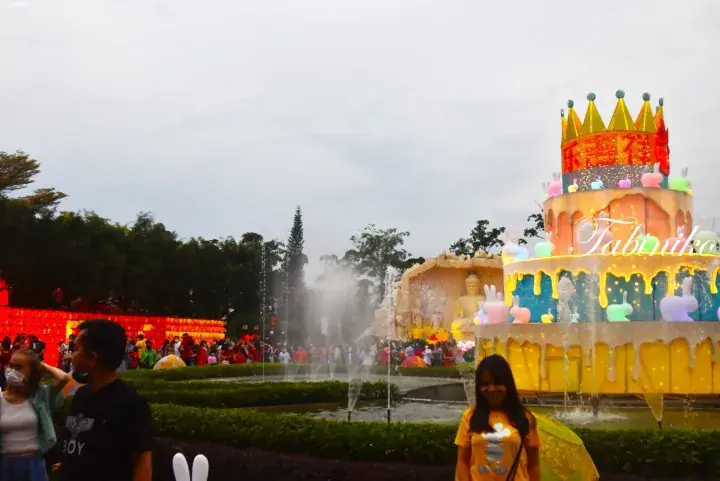 Large illuminated birthday cake lantern with bunny decorations and fountain at a festive night market in Malaysia