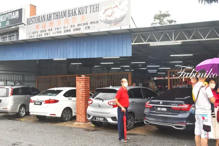 Ah Thiam Bak Kut Teh restaurant exterior with parked cars and customers waiting outside.