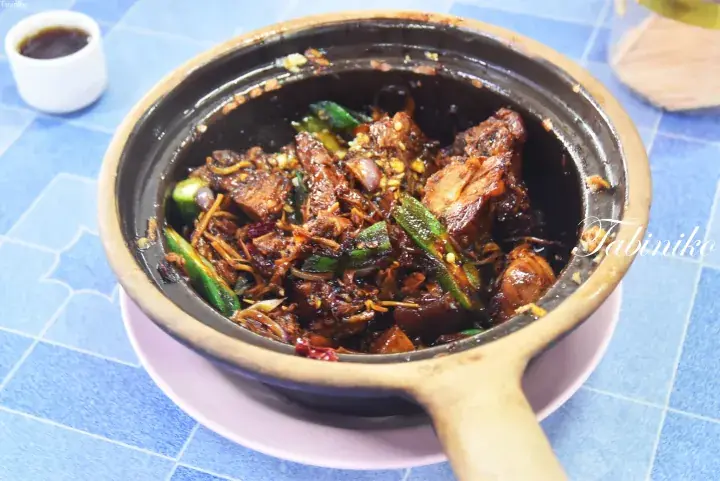 A claypot dish with braised meat and vegetables served on a blue tiled table.
