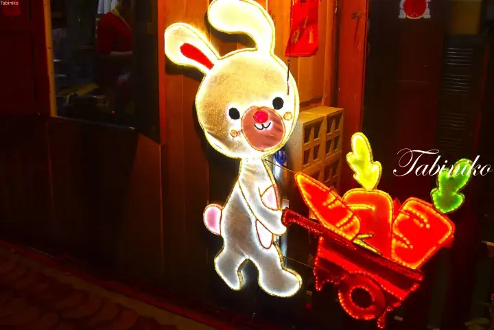 Illuminated rabbit lantern pushing a cart of carrots at a Malaysian night market.