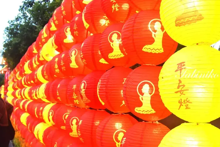 Rows of red and yellow lanterns with Buddha silhouettes and Chinese characters at a Malaysian temple festival.