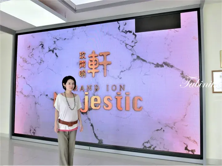 A woman stands in front of a large LED screen displaying the name ‘Grand Ion Jestic’ and Chinese characters.