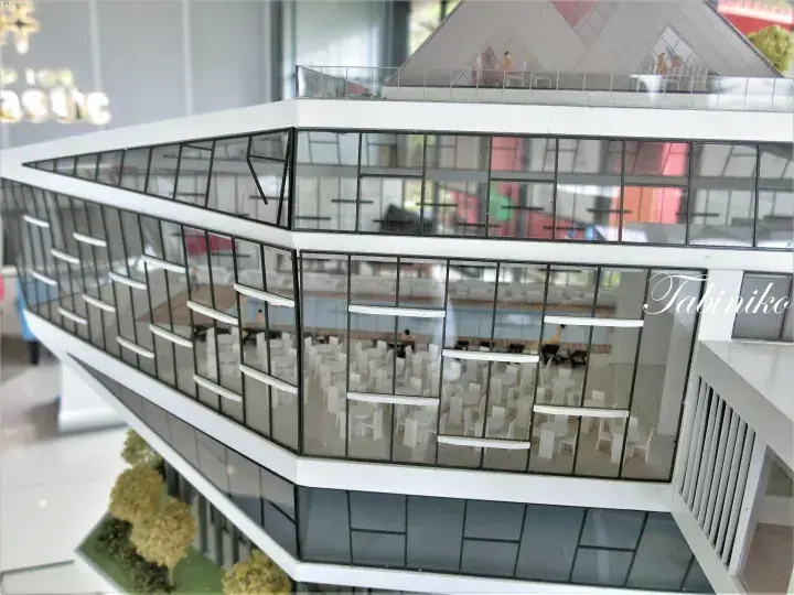 Architectural model of a modern glass-fronted building with white furniture visible inside.