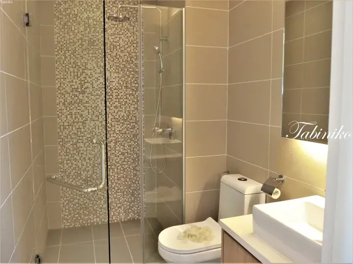 Modern hotel bathroom with beige tiles, glass shower enclosure, and white sink.