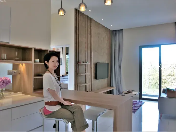 Woman sitting at a modern kitchen island in a stylish Malaysia property with wooden accents and a garden view.