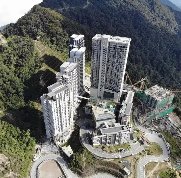 Aerial view of modern high-rise residential towers nestled in a lush green mountain landscape in Malaysia.