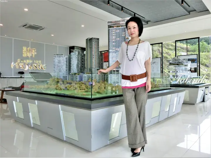 Woman standing beside a large architectural model of Grand Ion Majestic condominium at the sales gallery.