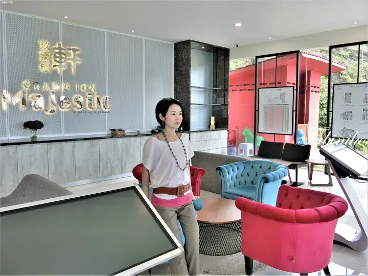 Woman standing in the Grand Ion Majestic sales gallery lobby with colorful furniture and property plans.