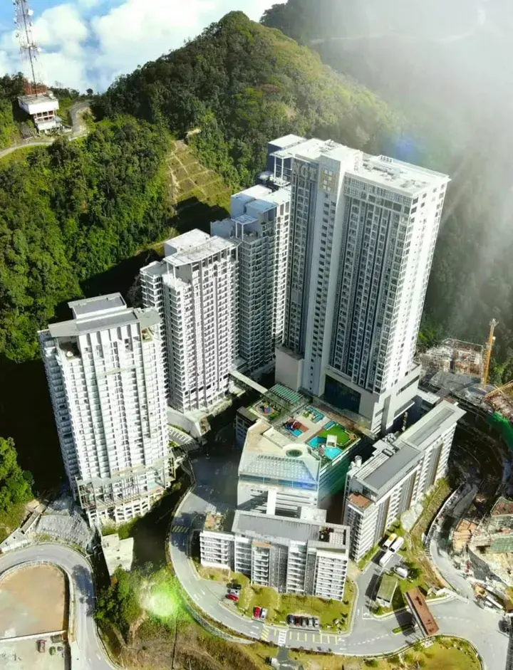 Aerial view of NCT Hilltop Resort in Fraser’s Hill, Malaysia, showcasing white high-rise buildings nestled in lush green hills.