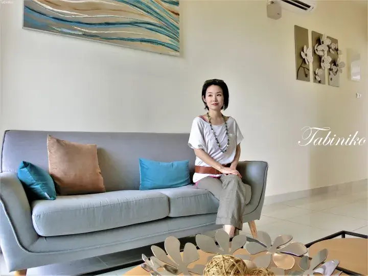 Woman sitting on a grey sofa in a modern living room with abstract wall art and decorative pillows.