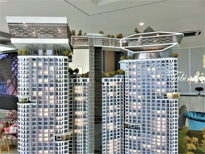 Architectural model of a modern high-rise residential complex featuring a skybridge connecting two towers with illuminated windows.