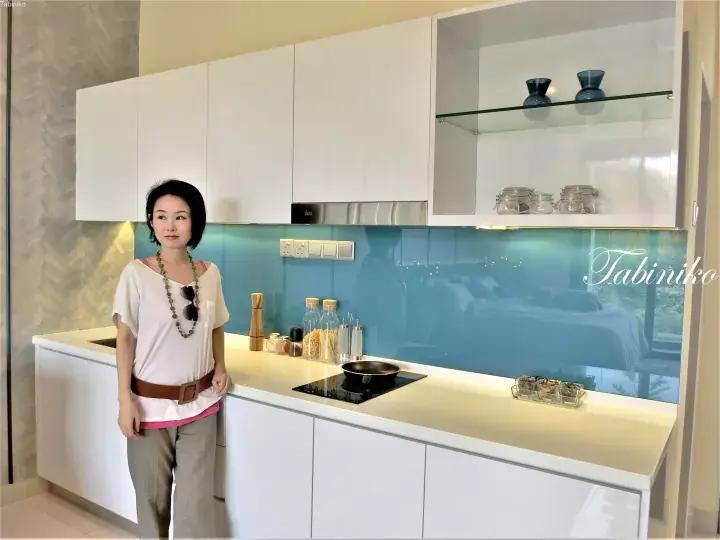 Woman standing in a modern kitchen with white cabinets and a blue glass backsplash.