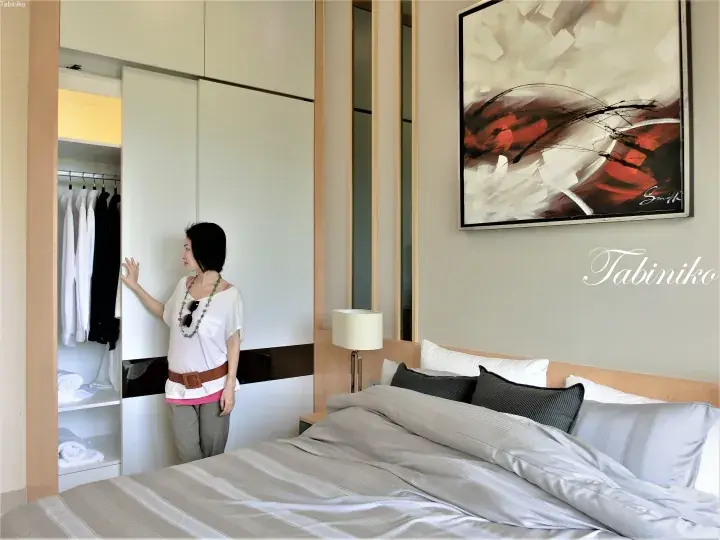 Woman opening a modern white wardrobe in a stylish hotel bedroom with abstract art.