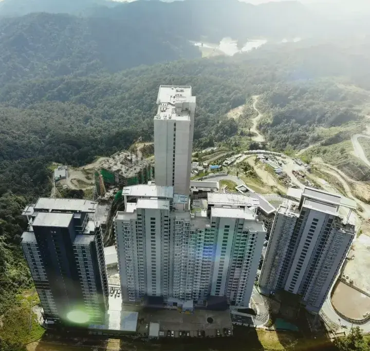 Aerial view of high-rise residential towers under construction in a lush, mountainous Malaysian landscape.