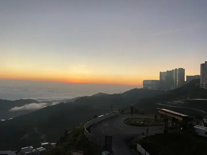 Sunrise over Genting Highlands with sea of clouds and resort buildings on the hillside.