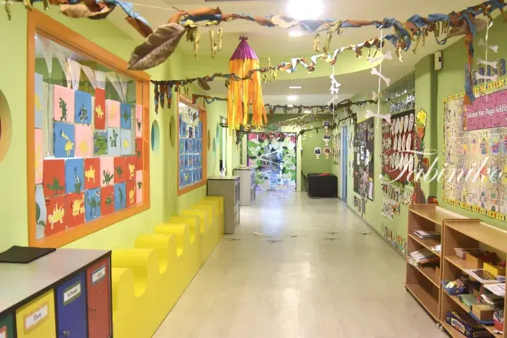 Colorful kindergarten hallway with dinosaur artwork, hanging decorations, and student cubbies.