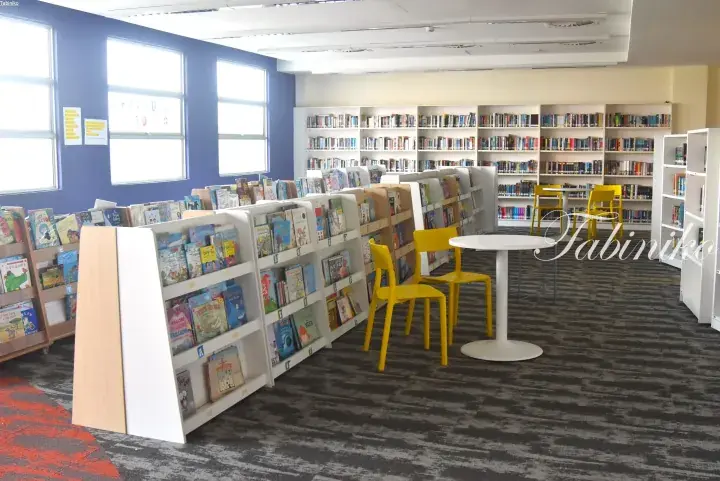 Bright children’s library with colorful bookshelves, yellow chairs, and white tables in a modern reading space.