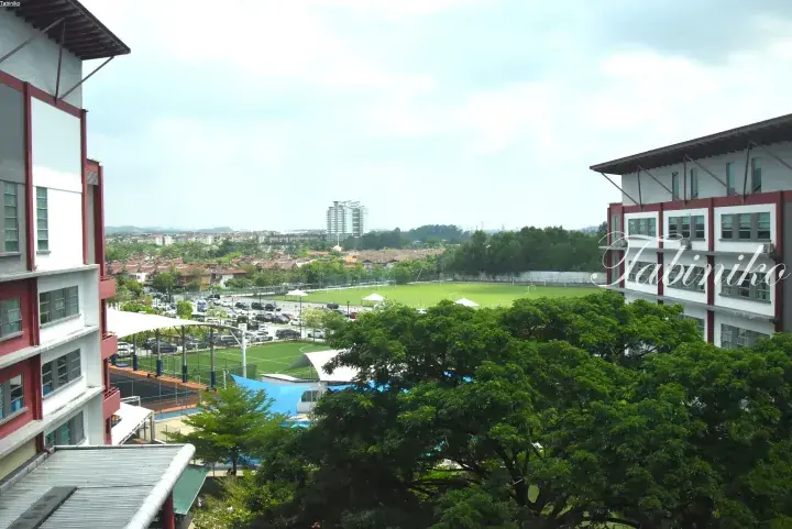 View of a school campus with sports fields, surrounded by residential areas and a high-rise building in the distance.