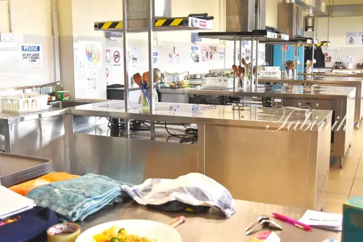Stainless steel kitchen counters with cooking utensils and signage in a commercial kitchen.