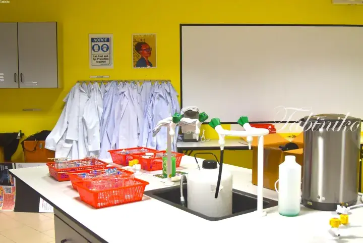 Laboratory setup with lab coats hanging on a yellow wall and science equipment on a white countertop.