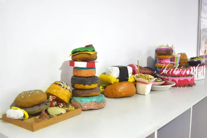 Colorful handmade clay models of burgers, donuts, sushi, and cakes arranged on a white table.