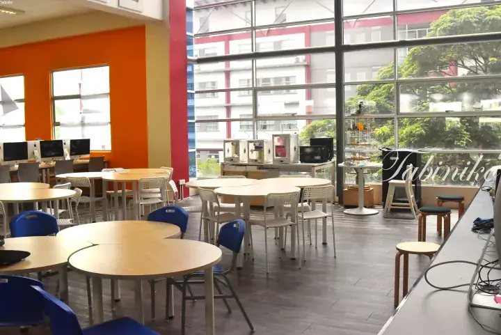 Bright co-working space with round tables, 3D printers, and large windows overlooking greenery.