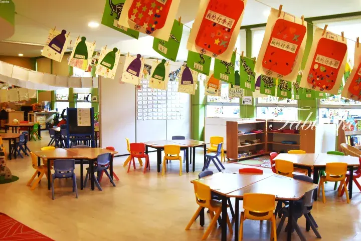 Colorful children’s classroom with small tables, chairs, and student artwork hanging from the ceiling.