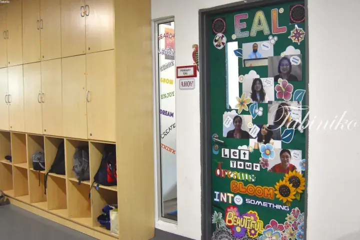 Primary EAL classroom door decorated with motivational quotes and teacher photos, next to wooden lockers in a school hallway.