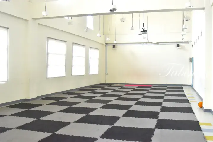 Spacious activity room with black and grey checkered mats, white walls, and large windows.