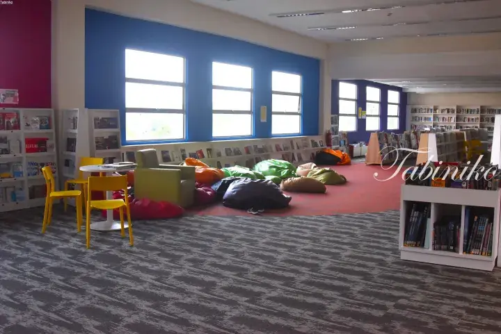 Modern library interior with colorful bean bags, yellow chairs, and bookshelves near large windows.
