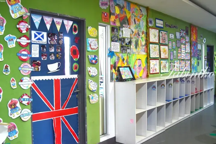 Green classroom hallway decorated with UK flags and children’s artwork, featuring white storage cubbies along the wall.