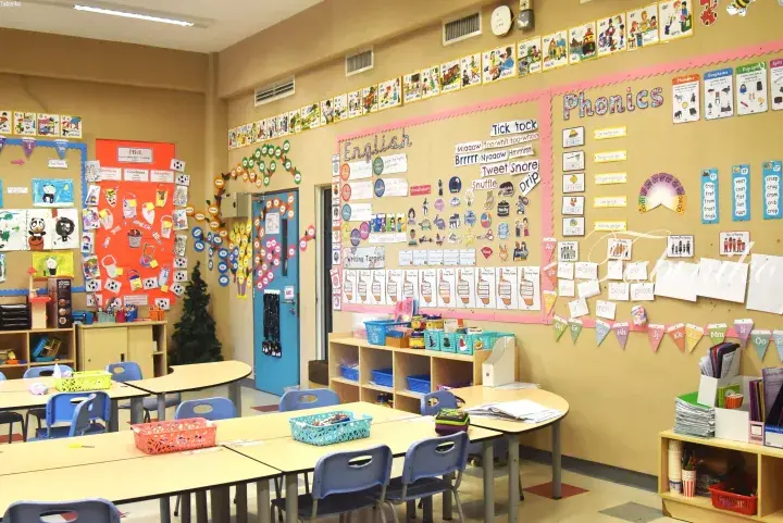 Bright classroom with colorful phonics and English learning displays on the walls, student desks, and educational materials.