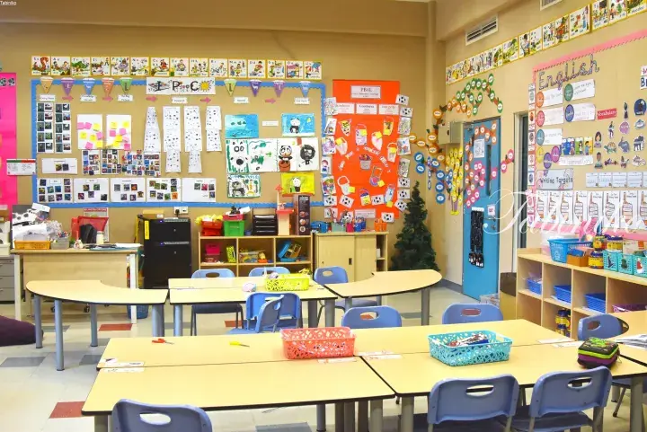 Bright classroom with student artwork, learning displays, and colorful tables and chairs arranged for group activities.