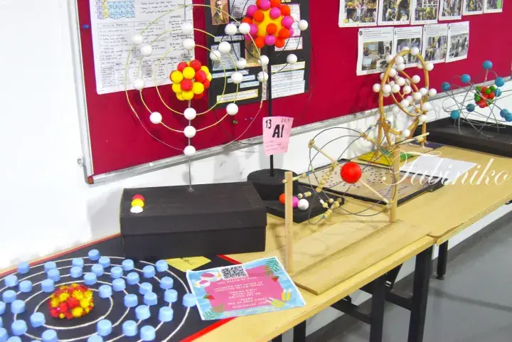 Educational models of atomic structures and periodic table elements displayed on a classroom table.
