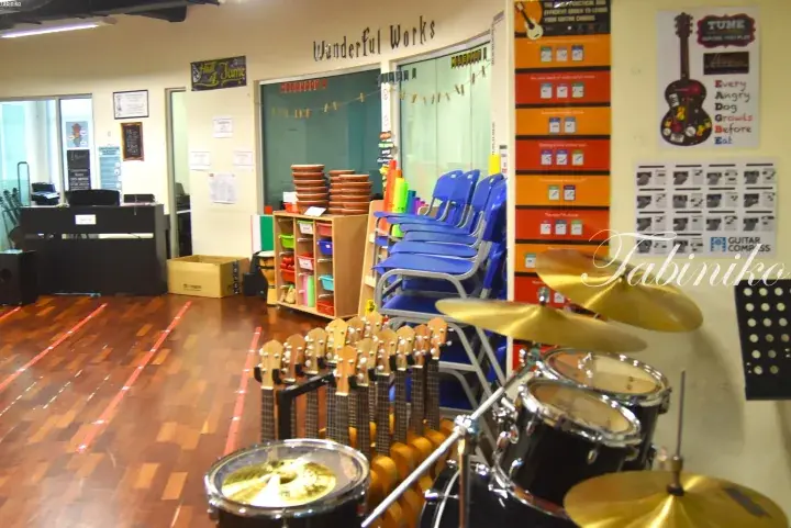 Music classroom with guitars, drums, and blue chairs in a bright room with wooden floors.