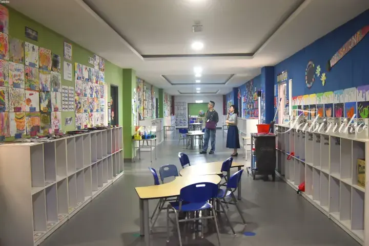 Colorful children’s art displayed on green and blue walls in a bright school corridor with student tables.