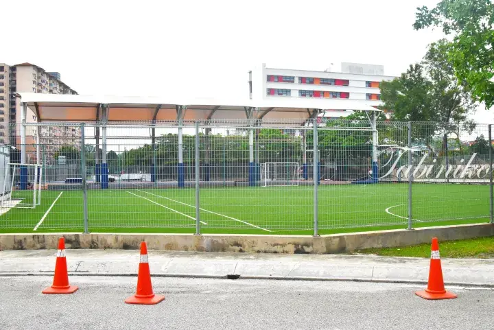 Fenced artificial turf football pitch with white canopy and orange traffic cones outside.