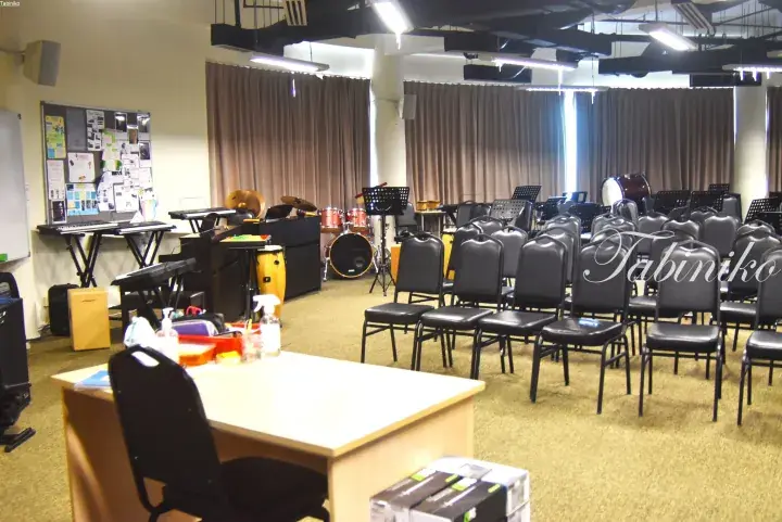 Spacious music classroom with rows of black chairs, keyboards, drums, and a teacher’s desk in a modern facility.