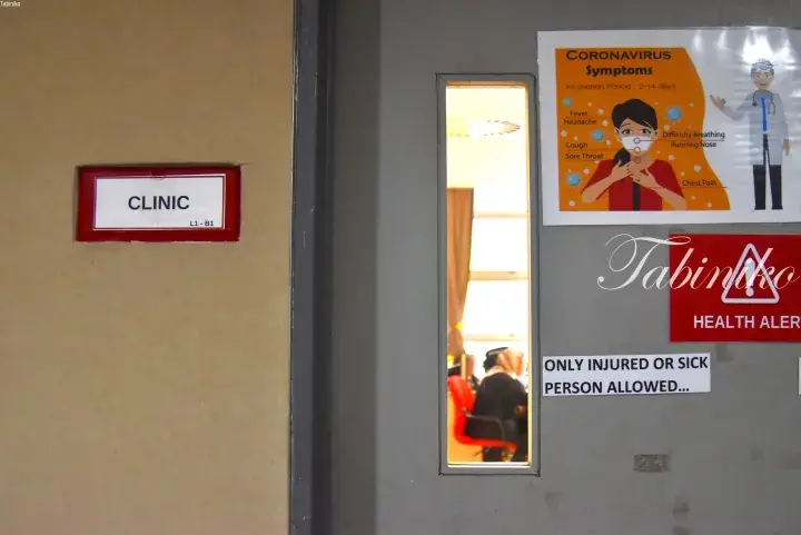 Clinic entrance with a red sign and a poster detailing coronavirus symptoms and health alert notices.