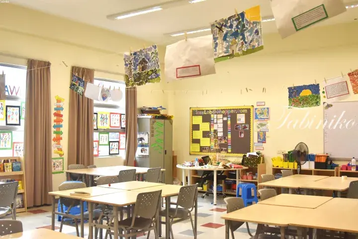 Bright classroom with student artwork hanging from the ceiling and desks arranged in groups.
