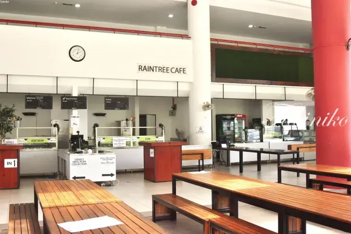 Raintree Cafe dining area with wooden tables, benches, and food counters offering Western, Vegetarian, and Asian options.