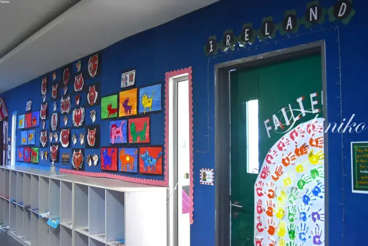 Colorful children’s artwork and handprints decorate a blue hallway wall with an Ireland-themed entrance.