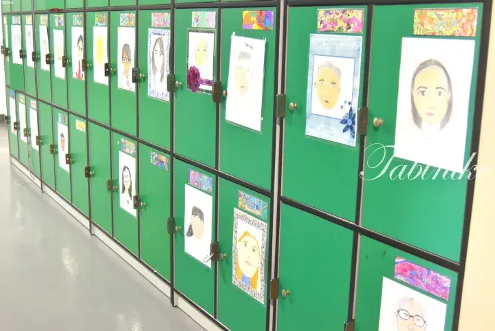 Green school lockers decorated with students’ colorful self-portrait drawings in a hallway.