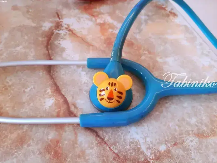 Blue toy stethoscope with a cute tiger face on the chest piece, resting on a marble surface.