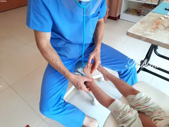 Doctor in blue scrubs examining a child’s foot in a clinic.