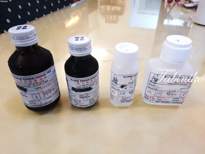 Four medicine bottles with handwritten labels from a Malaysian clinic sit on a glossy table.