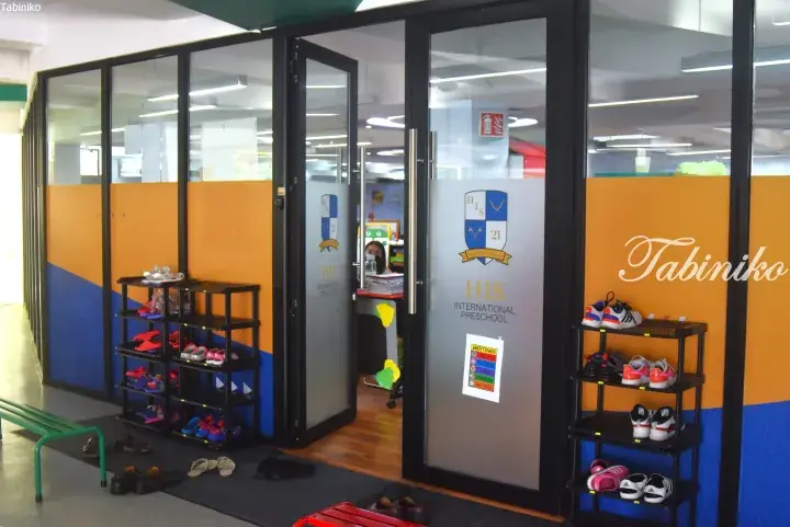 Entrance to HIS International Preschool with glass doors, shoe racks, and colorful orange and blue walls.