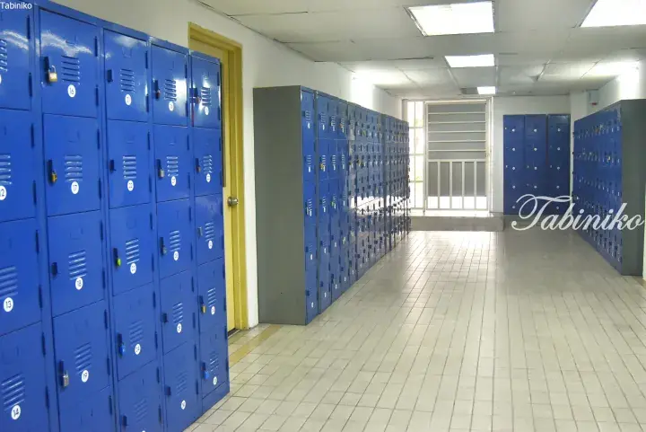 Rows of blue metal lockers in a school hallway with tiled floors and fluorescent lighting.