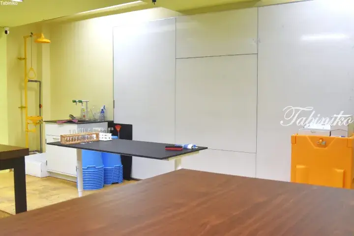Modern laboratory space featuring a black workbench, test tubes, and a yellow safety shower against a whiteboard wall.