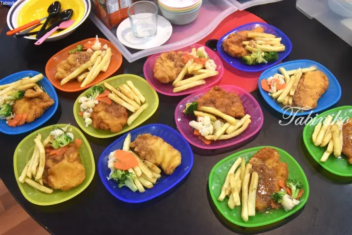 Colorful plates of fried chicken cutlet with french fries and steamed vegetables arranged on a dining table.